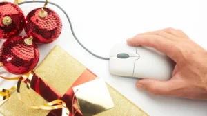 Gifting Guide - A mouse and hand, online shopping for Christmas presents, next to three red baubles and a Christmas present wrapped in gold paper.